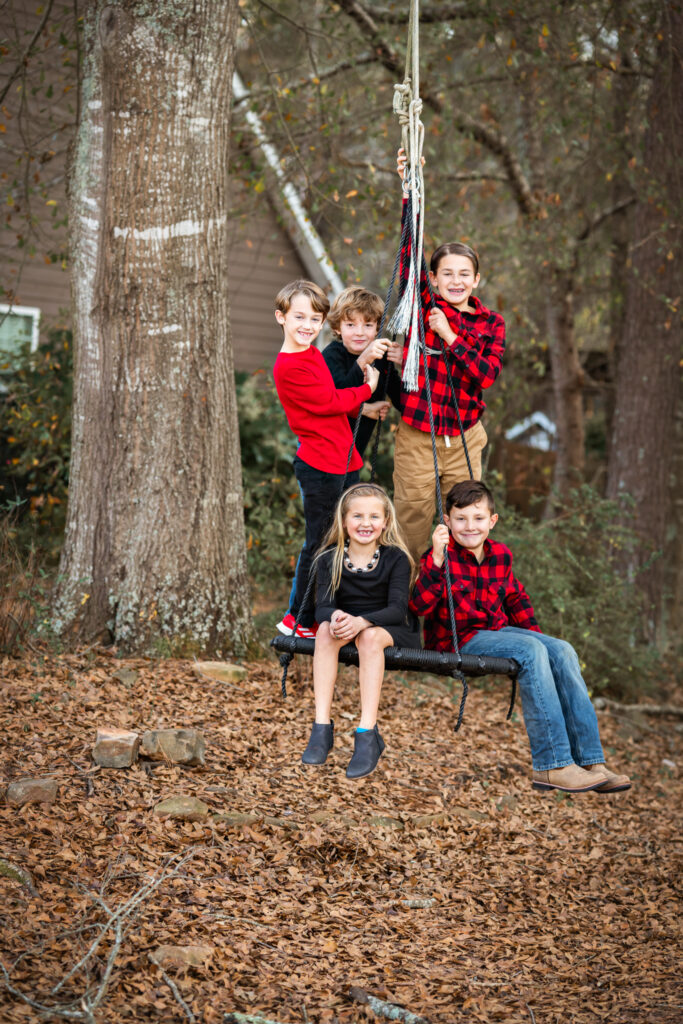 5 young children dressed in red are all piled up on a playset swing at their home in Peachtree City.