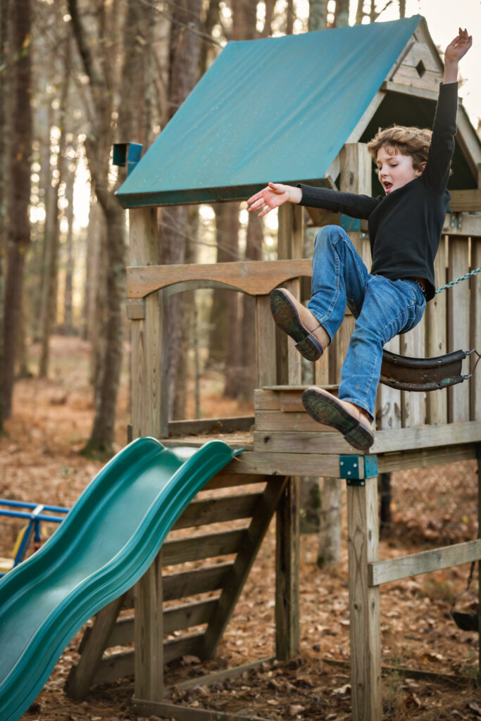 A young boy in a black sweater is flying through the air after jumping off a swing. 