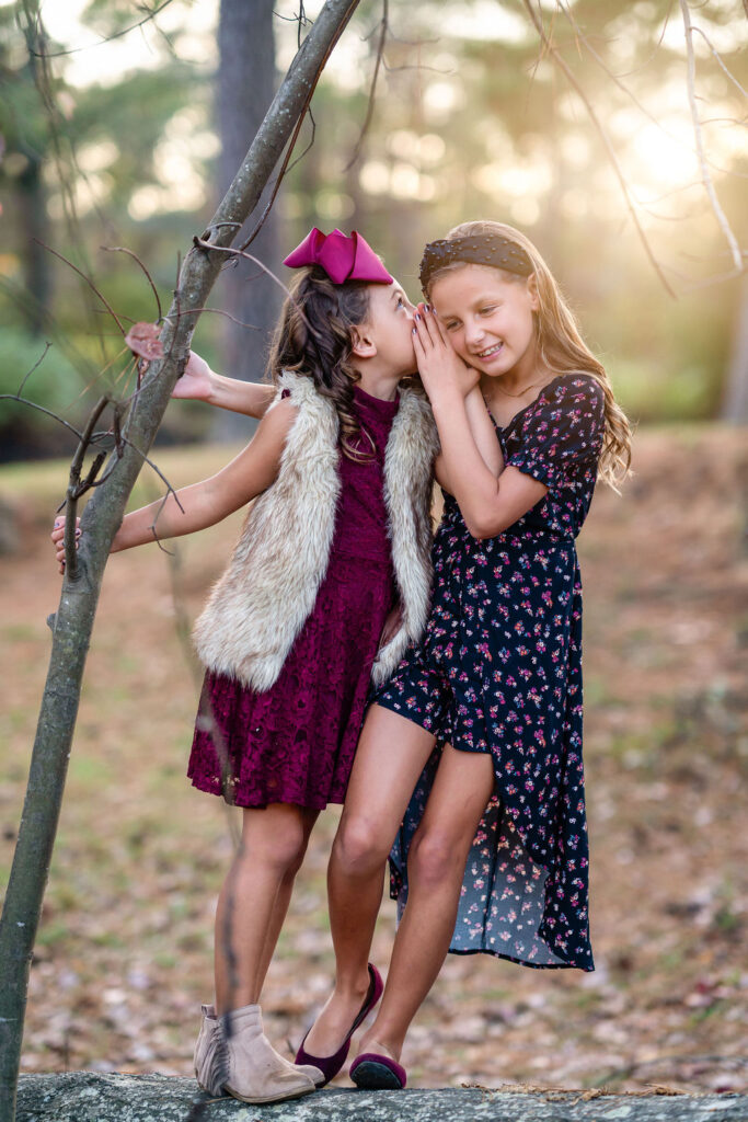 Two young sisters are standing on a tree trunk in Starr's Mill Park in Newnan GA.
