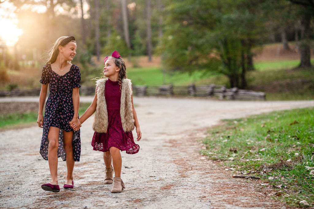 Two young sisters are holding hands as they walk through Starr's Mill Park during their photography session in Newnan, GA.