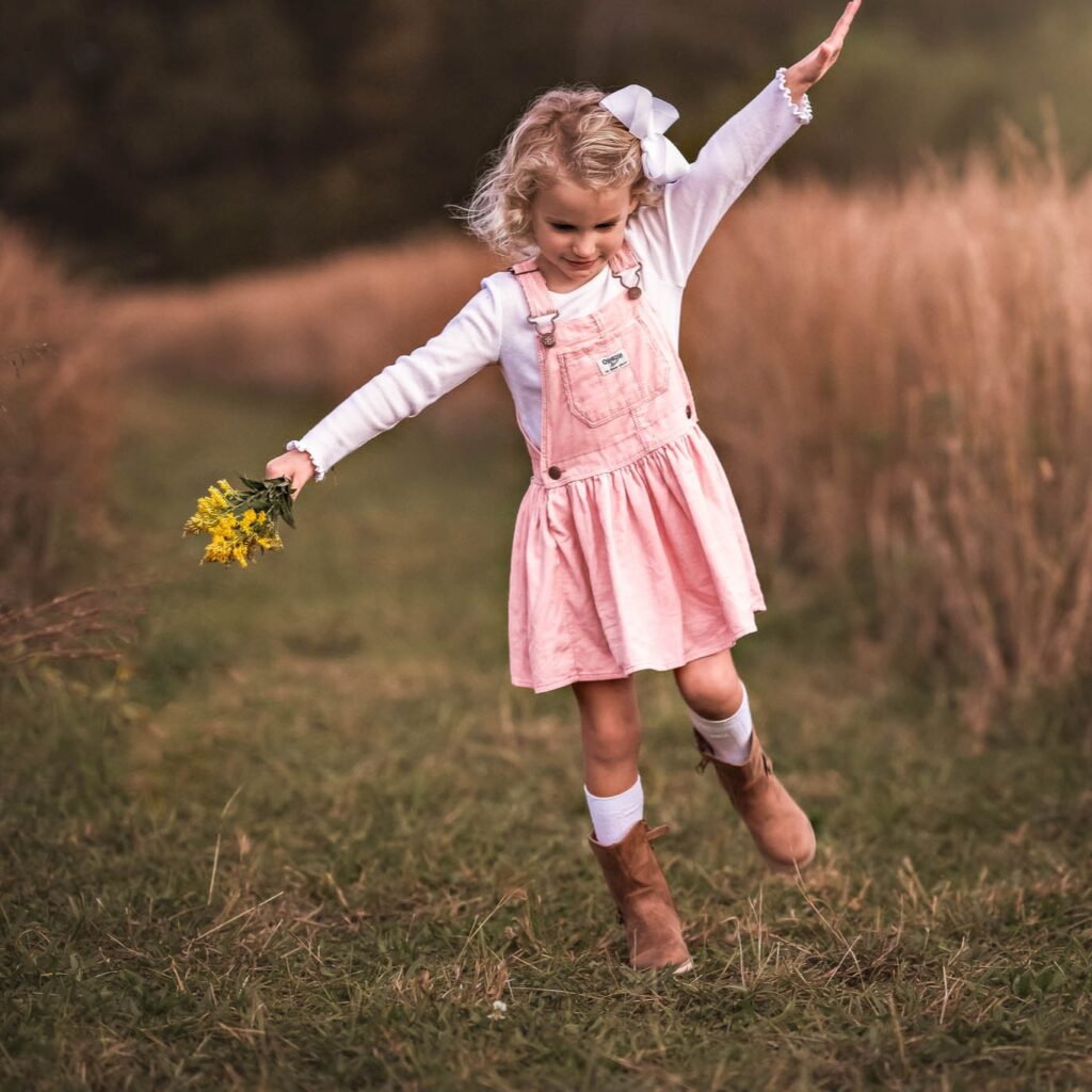 A young blonde girl is holding yellow flowers and walking through a field in Newnan, GA. 