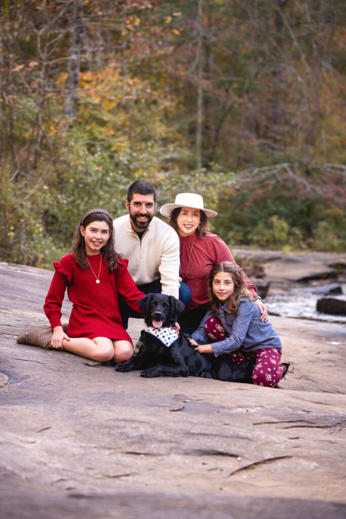 A family of four is sitting on a rock with their black lab dog. 